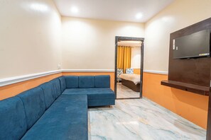 Habitación con sofá modular, cama con cortina amarilla, televisor montado en la pared y suelo de mármol.