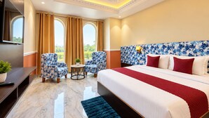 A hotel room with a bed, two armchairs, a small table, a TV, and a window with curtains.