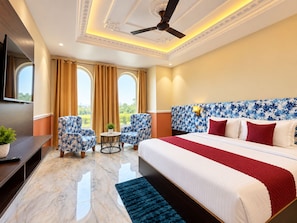 A hotel room with a bed, two armchairs, a small table, a TV, and a window with curtains. - Shree Maa Vaishno Hotel & Resort (Ujjain)
