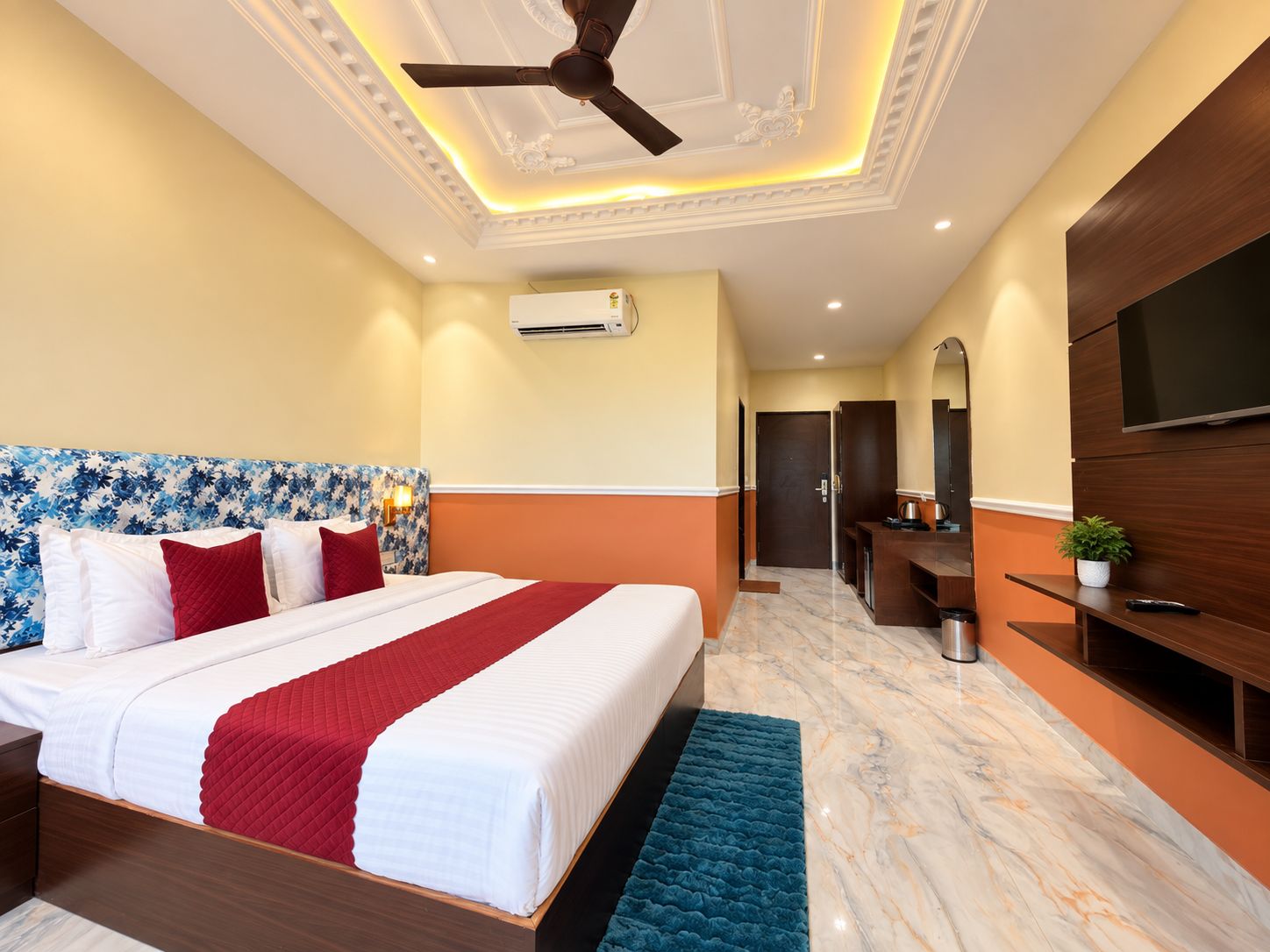 Ein Hotelzimmer mit Bett, Deckenventilator, Klimaanlage, Fernseher, Schreibtisch und Spiegel.