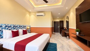 A hotel room with a bed, a ceiling fan, an air conditioning unit, a TV, a desk, and a mirror.