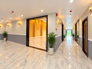 Un couloir d’hôtel avec un sol en marbre, des plantes en pot et des luminaires fixés au mur.