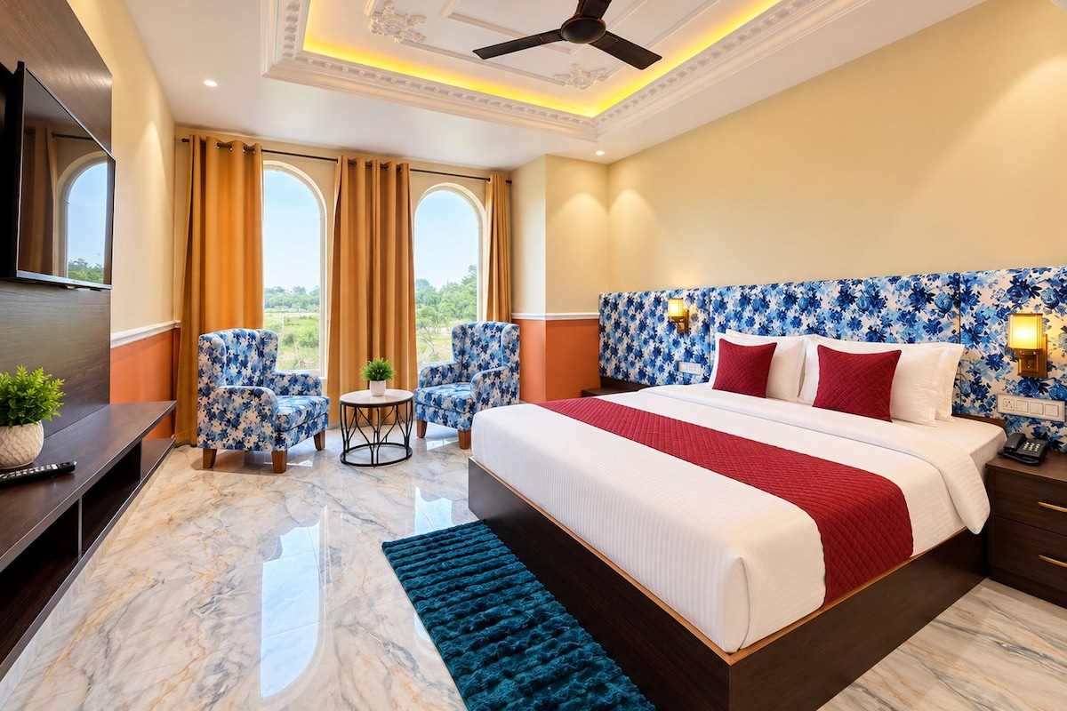 A hotel room with a large bed, two armchairs, a small table, and a TV.