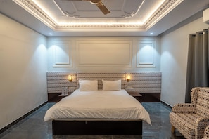 Una habitación de hotel con una cama grande, un cabecero estampado, dos lámparas de noche y un sillón con diseño.