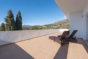 Un balcon donnant sur un paysage montagneux, deux fauteuils de jardin en osier et une petite table.