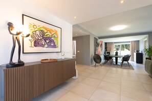A modern living room with a dining area, featuring a wooden console table, a colorful abstract painting, and a large window with curtains. - Villa Linn - Modern Family Villa in Mijas (Mijas)