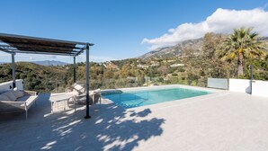 Ein Pool auf dem Dach mit einer Pergola und einer Sitzgelegenheit, umgeben von einer gebirgigen Landschaft.