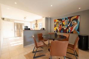 A modern kitchen with stainless steel appliances, a dining area with a round table and leather chairs, and a large abstract painting on the wall. - Villa Linn - Modern Family Villa in Mijas (Mijas)