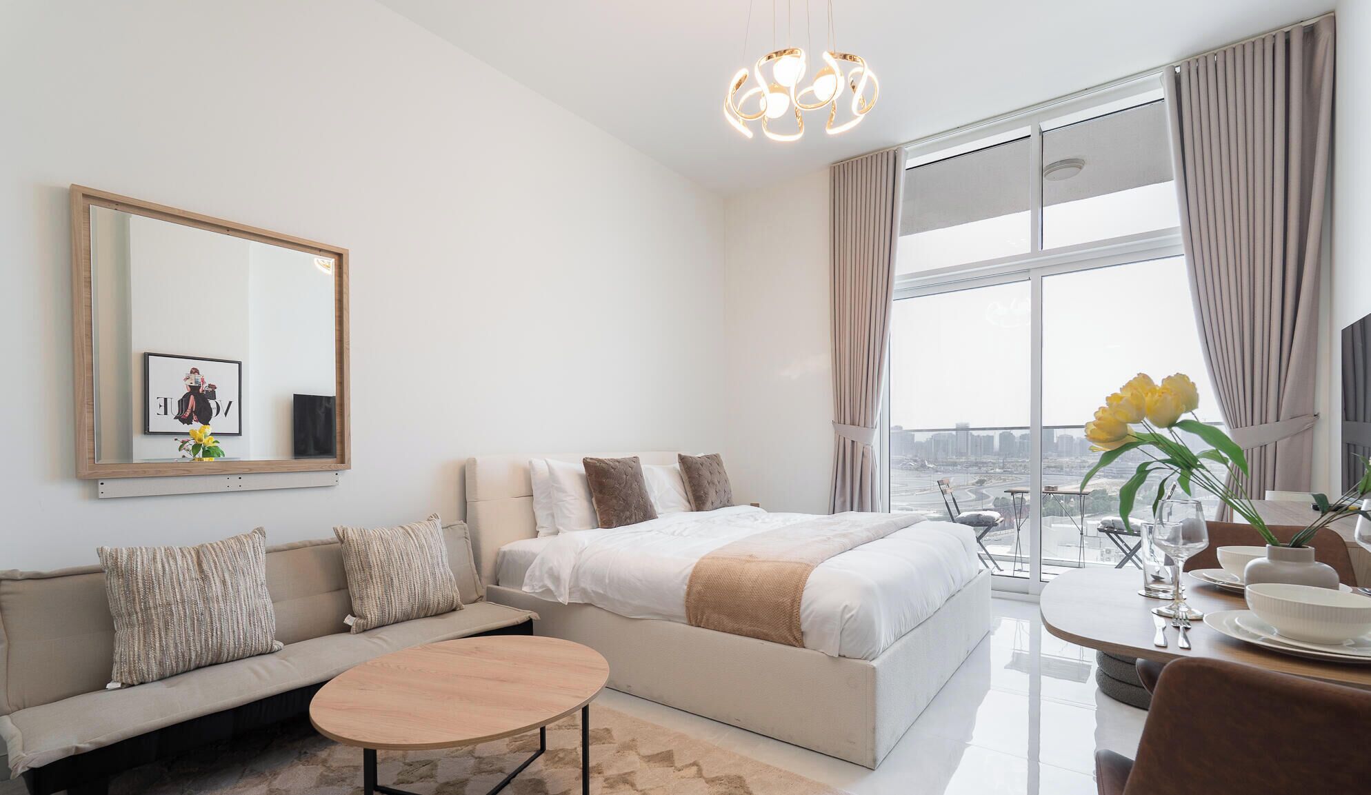 A modern hotel room with a large bed, a sofa, a dining table, and a view of the cityscape.