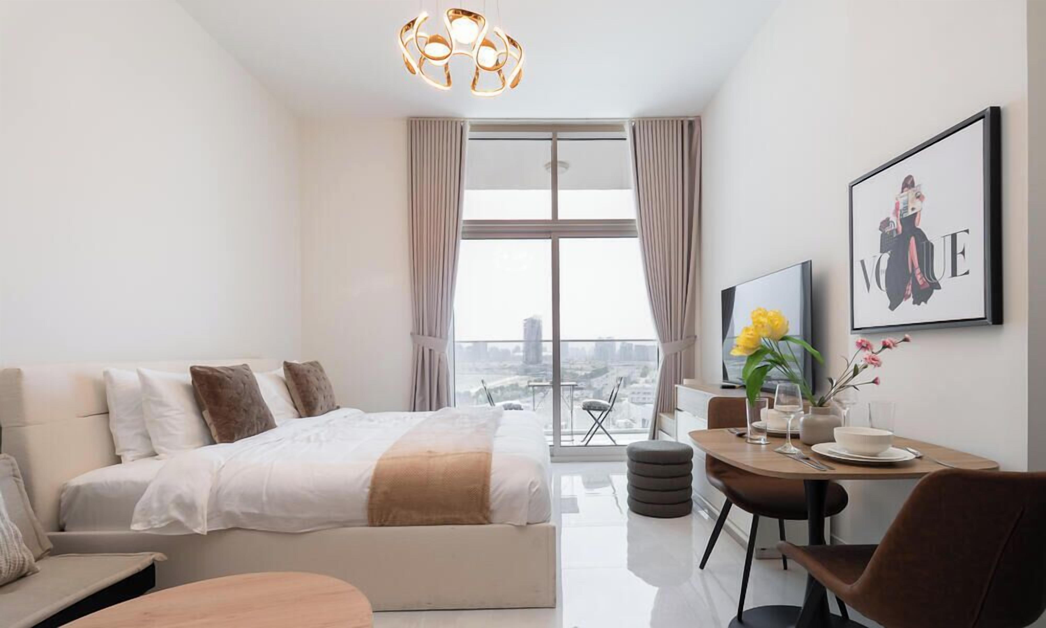 Quarto de hotel moderno com uma cama grande, um espaço de jantar e vista para a cidade.