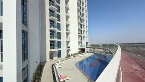 Un edificio moderno con zona de piscina en la azotea, que incluye sillas de descanso y una barandilla de cristal.