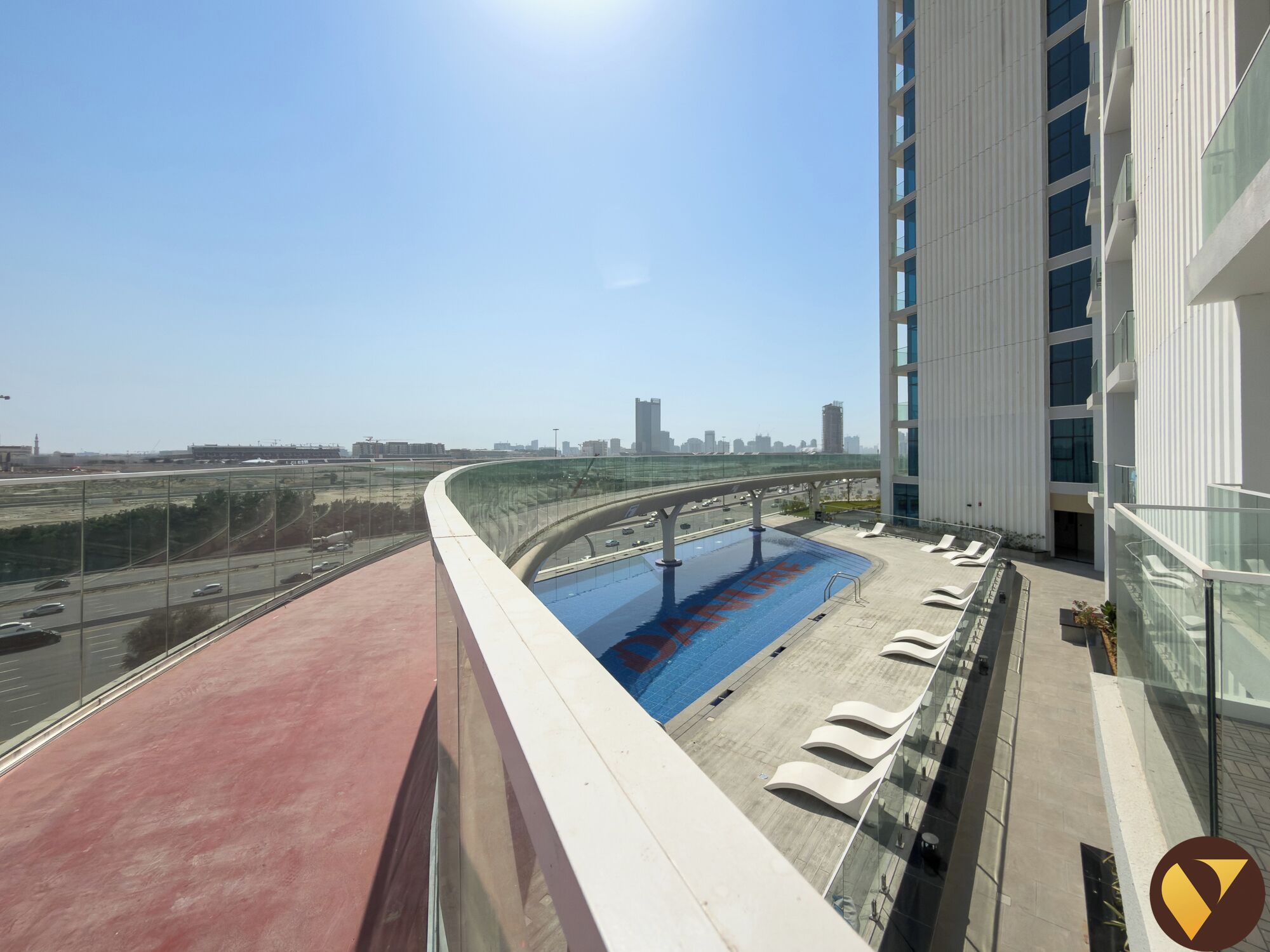Um edifício moderno com piscina no terraço, guarda-corpo de vidro e vista para o horizonte da cidade.