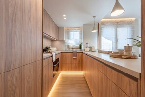 A modern kitchen with wooden cabinetry, a countertop, and a hanging light fixture. - Can Costelles II - Mediterranean Gem with Sea View (Cambrils)