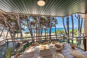 An outdoor dining area with a view of the beach and ocean, featuring a table set with plates, glasses, and a wooden bowl. - Can Costelles II - Mediterranean Gem with Sea View (Cambrils)