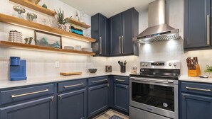 A modern kitchen with dark blue cabinets, stainless steel appliances, and wooden shelves with decorative items. - 1 Car Garage | Gourmet Kitchen | On Bus Route (Steamboat Springs)