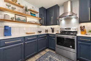 A modern kitchen with dark blue cabinets, stainless steel appliances, and wooden shelves with decorative items. - 1 Car Garage | Gourmet Kitchen | On Bus Route (Steamboat Springs)