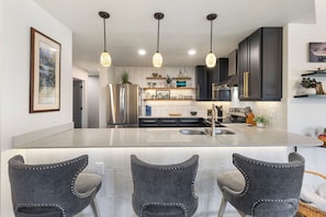 A modern kitchen with a central island, bar stools, pendant lighting, and dark cabinetry. - 1 Car Garage | Gourmet Kitchen | On Bus Route (Steamboat Springs)