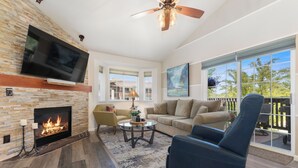 A living room with a fireplace, a television, a ceiling fan, and a large window with a view. - 1 Car Garage | Gourmet Kitchen | On Bus Route (Steamboat Springs)