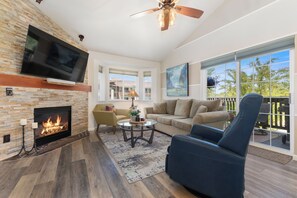 A living room with a fireplace, a television, a ceiling fan, and a large window with a view. - 1 Car Garage | Gourmet Kitchen | On Bus Route (Steamboat Springs)