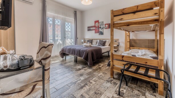 A room with a bunk bed, a desk with a chair, a bed with pillows, a wall-mounted TV, and a window with curtains. - THAT'S AMORE FIUMICINO AIRPORT  (Fiumicino)