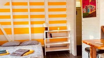 Une pièce comprenant un lit, une petite table, une étagère avec des livres et un tableau accroché au mur.