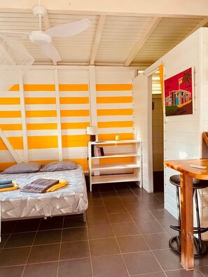 A room with a bed, a small table, a shelf with books, and a painting on the wall. - Kaz Kokonut, a Creole bungalow on Marie-Galante (Saint-Louis)