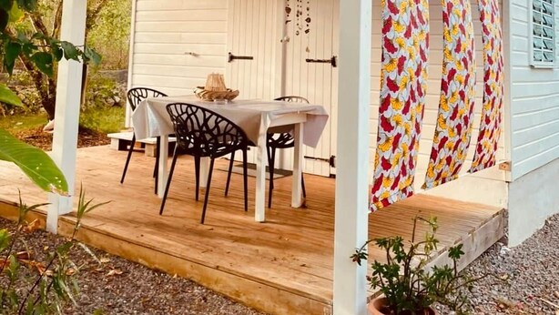 A covered outdoor seating area with a table and chairs, a potted plant, and a colorful curtain.