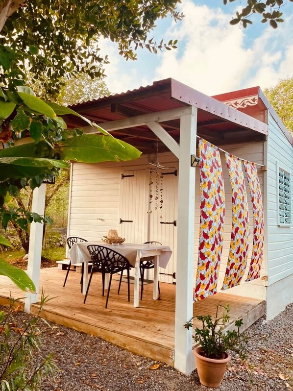 A covered outdoor seating area with a table and chairs, a potted plant, and a colorful curtain.