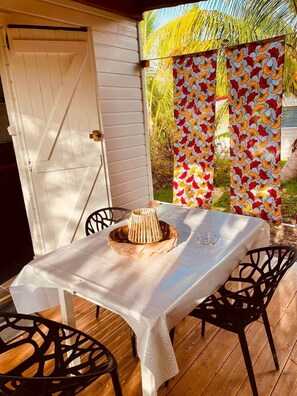 An outdoor dining area with a table covered by a white tablecloth, two black chairs, and a woven basket on the table.