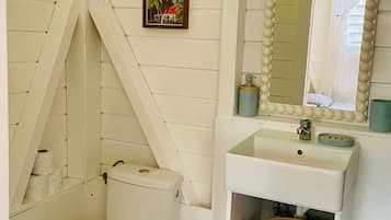 Une salle de bain comprenant des toilettes, un lavabo, un miroir et une étagère avec des paniers de rangement.