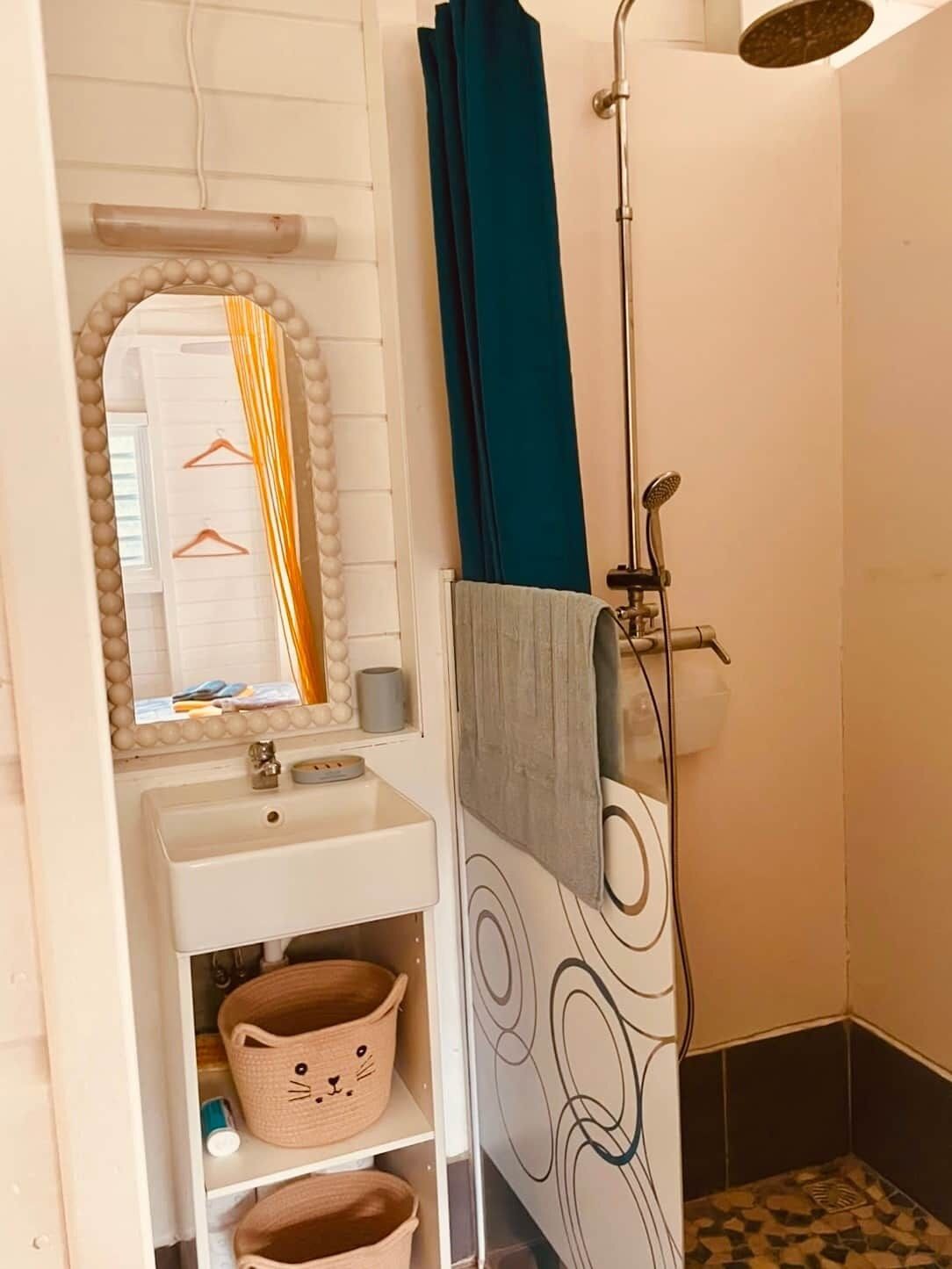 Une salle de bain avec un lavabo blanc, un miroir avec un cadre orné de perles, un porte-serviettes et une douche avec un rideau bleu.