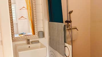 Une salle de bain avec un lavabo blanc, un miroir avec un cadre orné de perles, un porte-serviettes et une douche avec un rideau bleu.