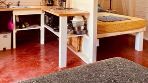 A compact, open-plan room with a kitchenette, a bed with a yellow mattress, and a patterned rug. - Kaz Papaya, a Creole bungalow on Marie-Galante (Saint-Louis)