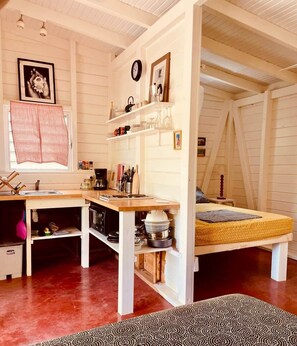 A compact, open-plan room with a kitchenette, a bed with a yellow mattress, and a patterned rug. - Kaz Papaya, a Creole bungalow on Marie-Galante (Saint-Louis)
