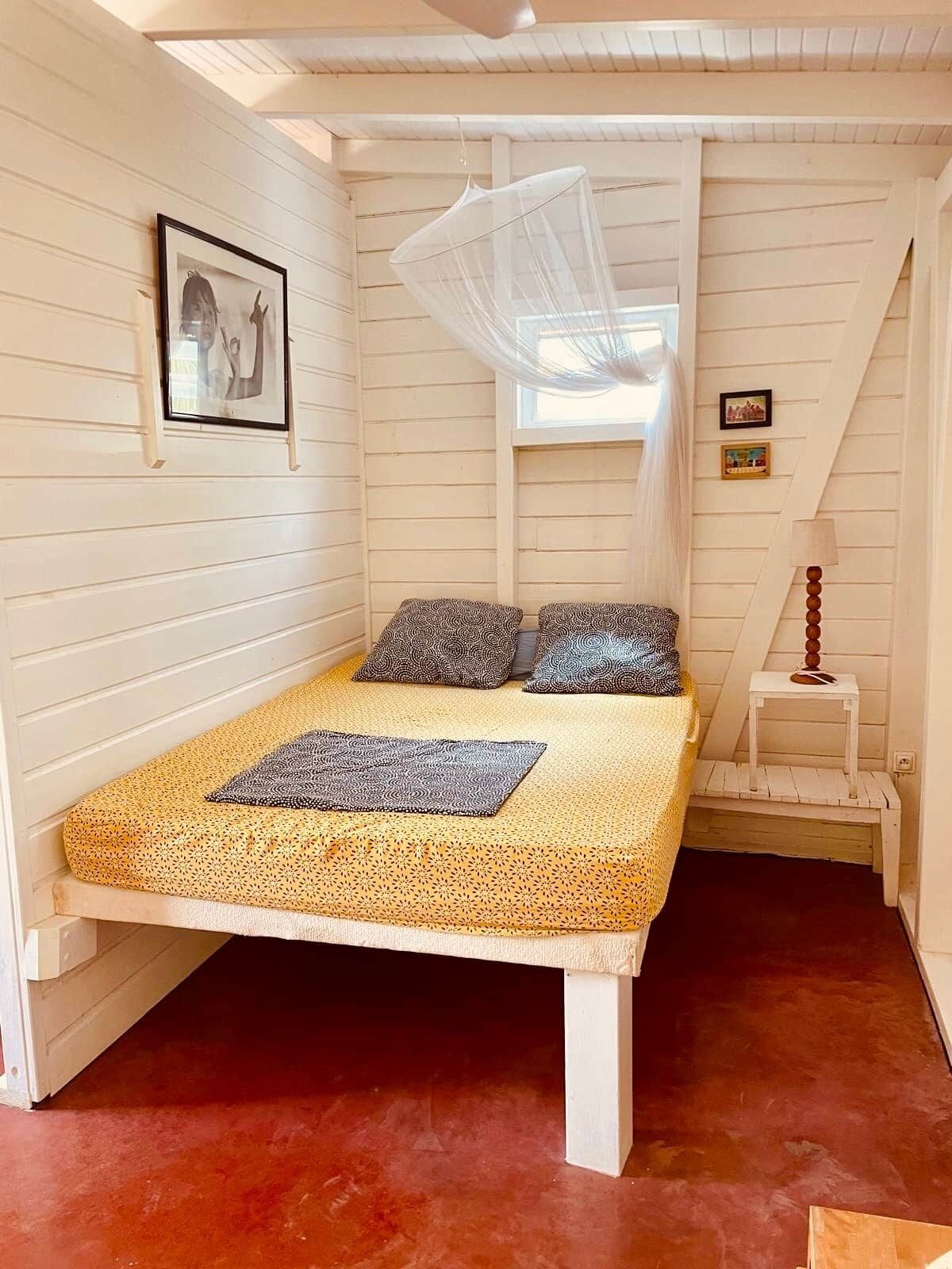 A bed with a canopy, two pillows, a bedside table, and a picture on the wall.