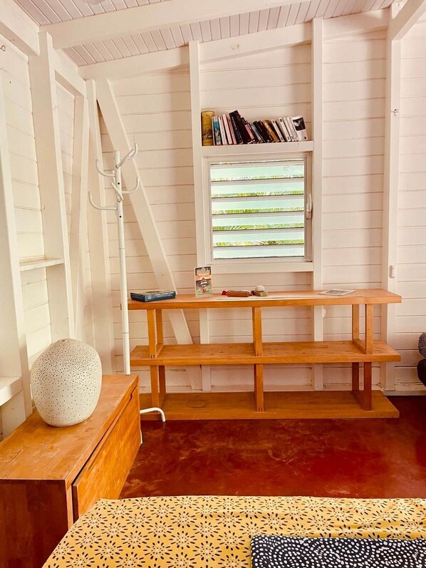 A room with a wooden bench, a coat rack, a small table with a vase, and a window with blinds.