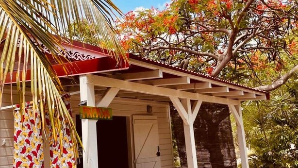 A covered porch with a wooden floor, a table and chairs, and a potted plant. - Kaz Papaya, a Creole bungalow on Marie-Galante (Saint-Louis)