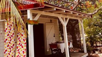 A covered porch with a wooden floor, a table and chairs, and a potted plant.