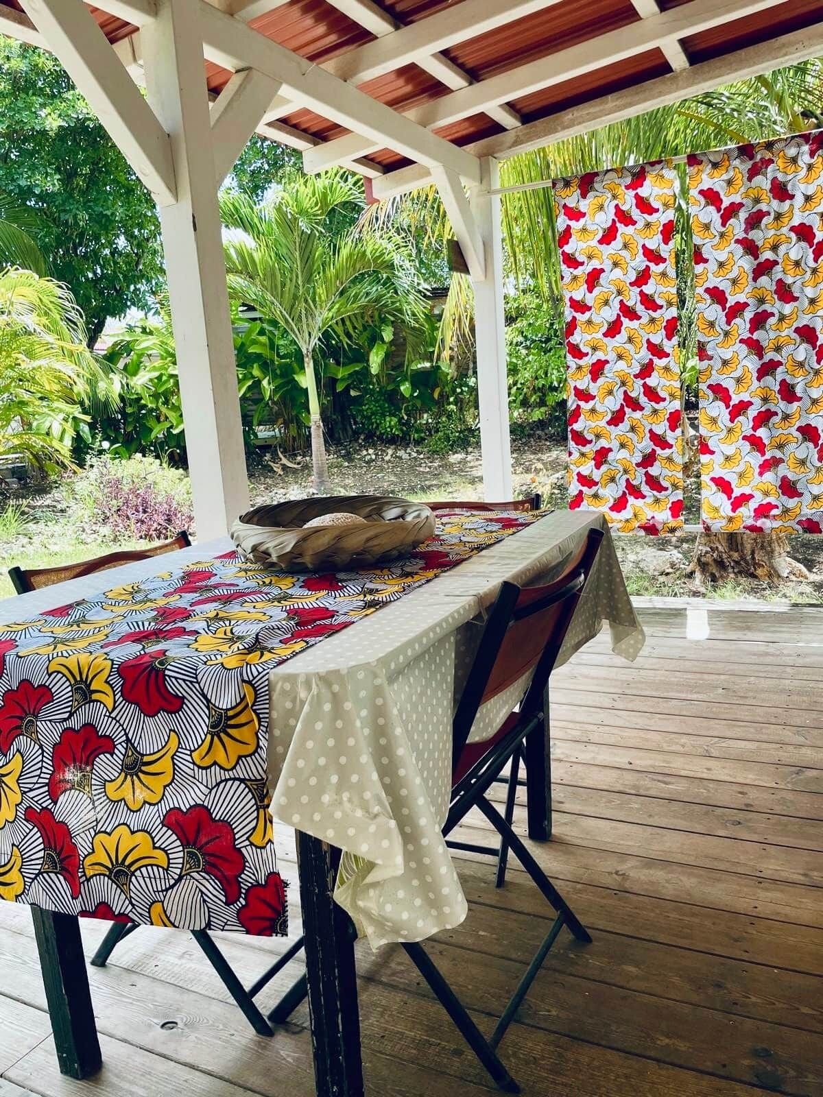 An outdoor dining area with a wooden deck, a covered section with a white ceiling, and a table set with a patterned tablecloth.