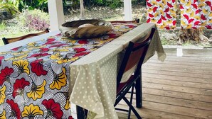 An outdoor dining area with a wooden deck, a covered section with a white ceiling, and a table set with a patterned tablecloth. - Kaz Papaya, a Creole bungalow on Marie-Galante (Saint-Louis)