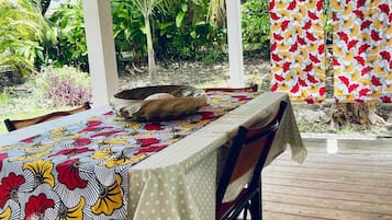 An outdoor dining area with a wooden deck, a covered section with a white ceiling, and a table set with a patterned tablecloth.