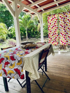 An outdoor dining area with a wooden deck, a covered section with a white ceiling, and a table set with a patterned tablecloth. - Kaz Papaya, a Creole bungalow on Marie-Galante (Saint-Louis)