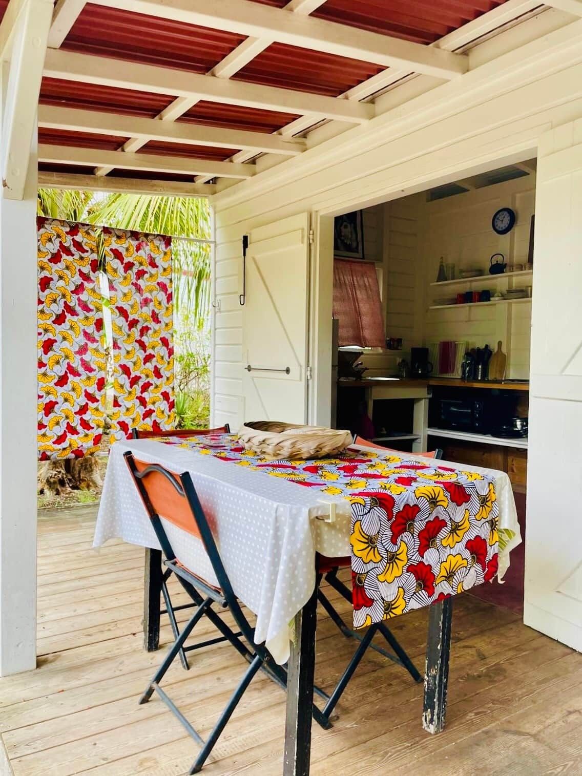 Ein Essbereich im Freien mit einem Tisch, der mit einer gemusterten Tischdecke bedeckt ist, einem Stuhl und einer Holzterrasse.