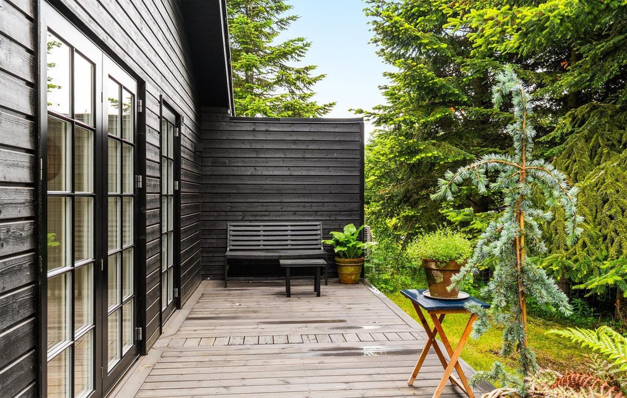 Une terrasse en bois avec un banc et des plantes en pot, entourée d’une végétation luxuriante.
