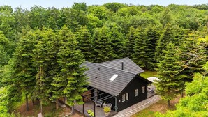 Une cabane entourée d’une forêt dense, dotée d’une terrasse et d’un espace salon extérieur.