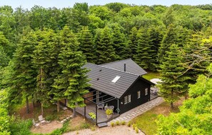 Eine Holzhütte, umgeben von dichtem Wald, mit einer Terrasse und Sitzgelegenheiten im Freien.