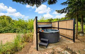 Ein Whirlpool mit einer Holzterrasse und einer kleinen Bank, umgeben von einem Holzzaun und Grünpflanzen.
