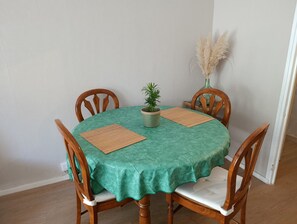 A round dining table with a green tablecloth, four wooden chairs, two placemats, and a potted plant. - Perfect 3-bedroom apartment in Saint-Herblain for your getaway (Saint-Herblain)