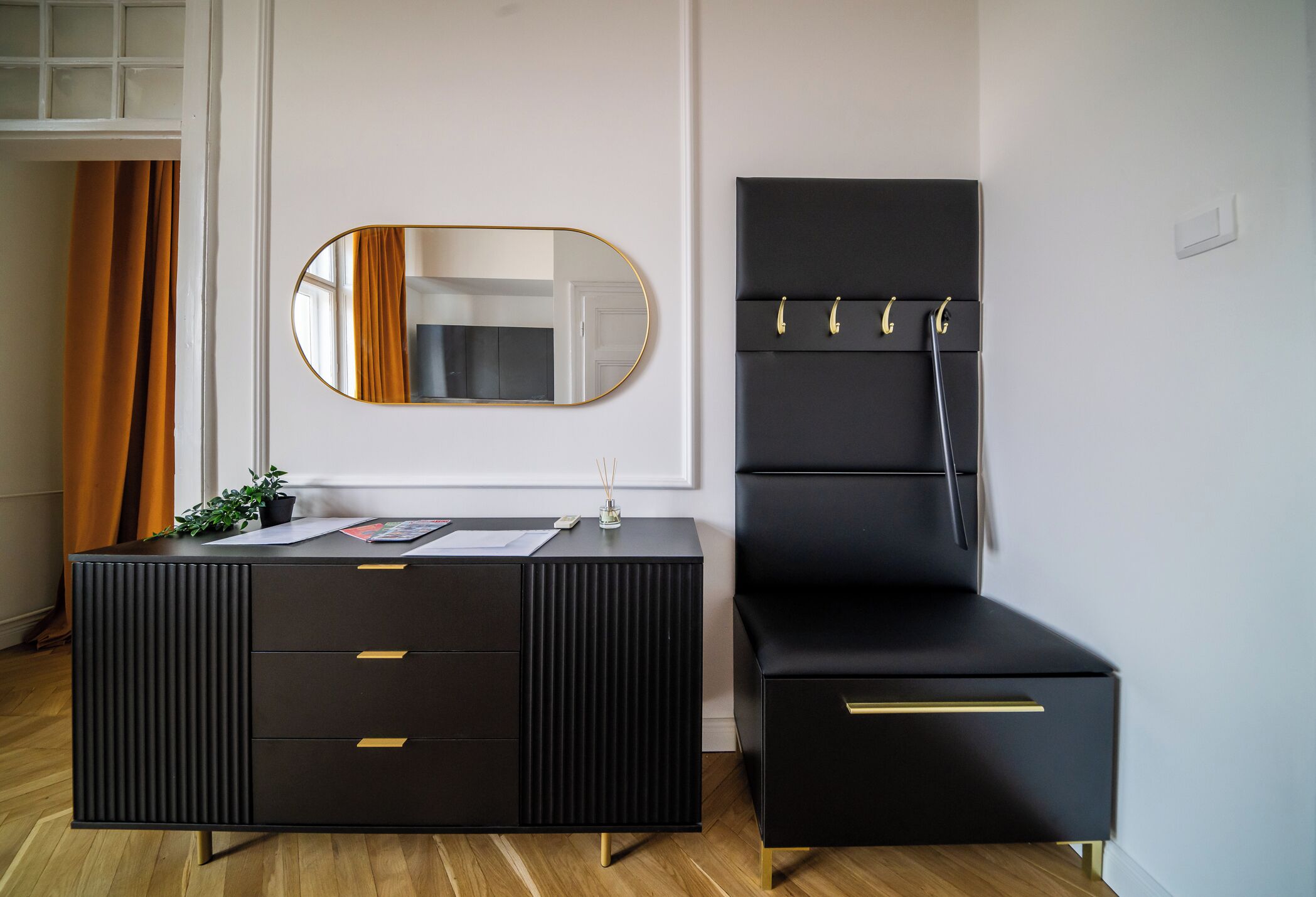 A black vanity with a mirror, a small table with a plant, and a black chair with hooks.
