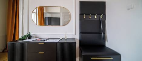 A black vanity with a mirror, a small table with a plant, and a black chair with hooks.